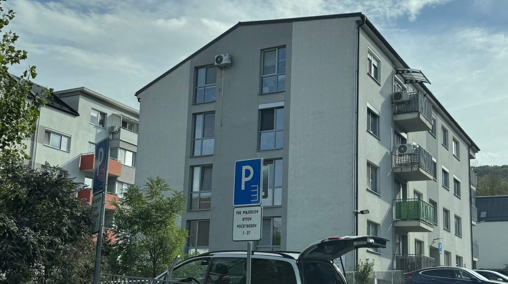 Pohľad na bytový dom v projekte Pod lesom v Devínskej Novej Vsi s vyhradeným parkovaním v popredí.