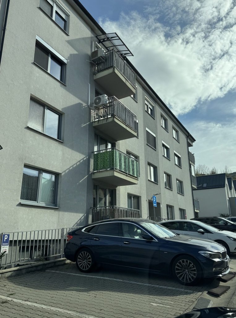 Širší záber na bytový dom a parkovacie státia v lokalite Pod lesom v Devínskej Novej Vsi.   